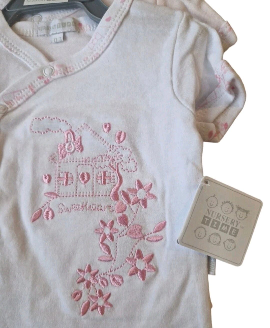 White baby onesie with pink floral design and 'Nursery Time' tag on a white background