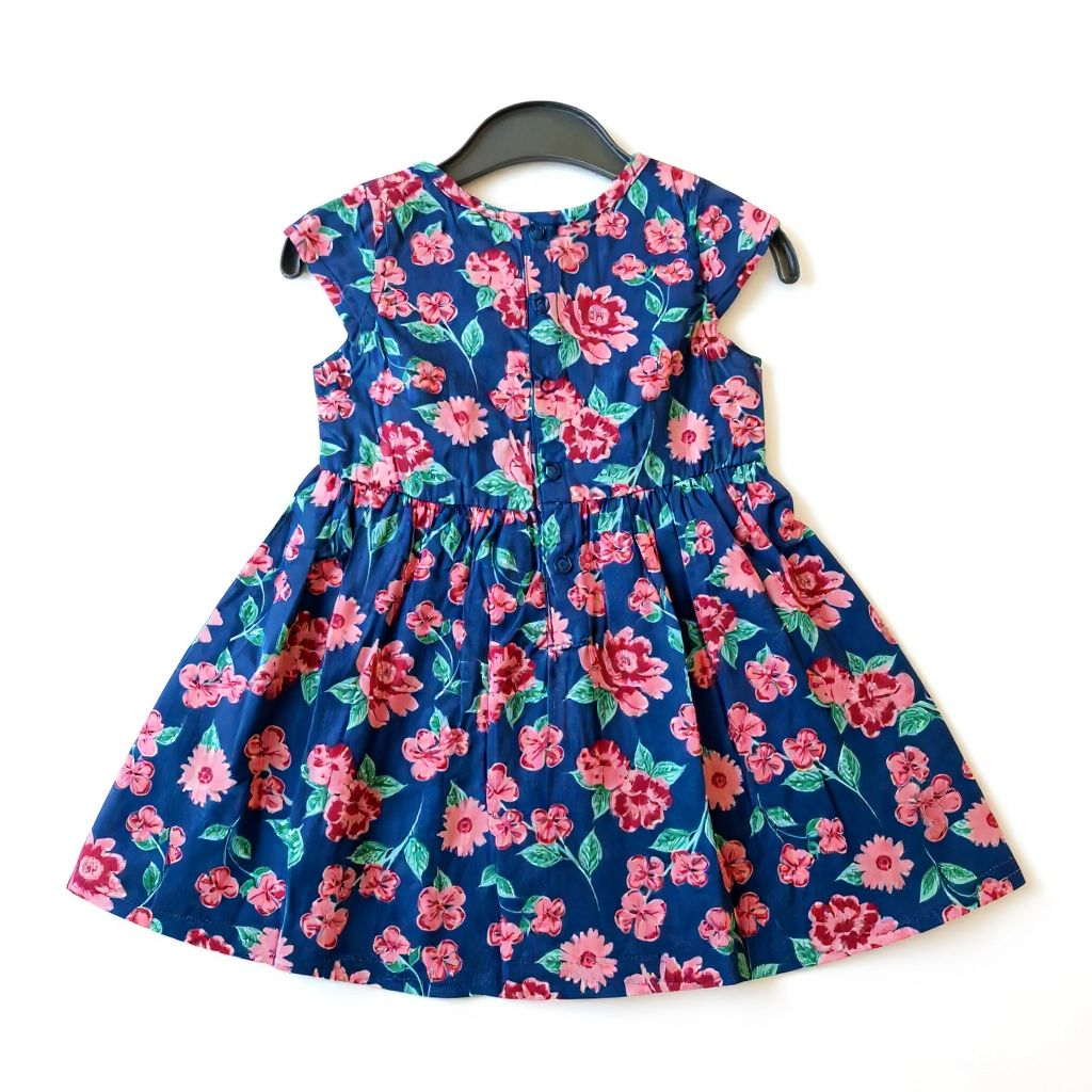 Floral dress with pink flowers on a blue background, hanging on a black hanger.