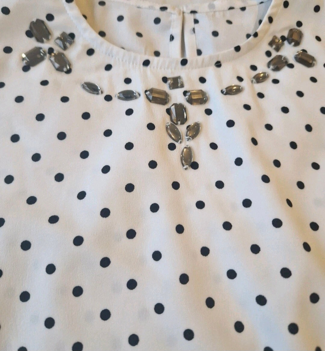 White blouse with black polka dots and silver embellishments on a plain background