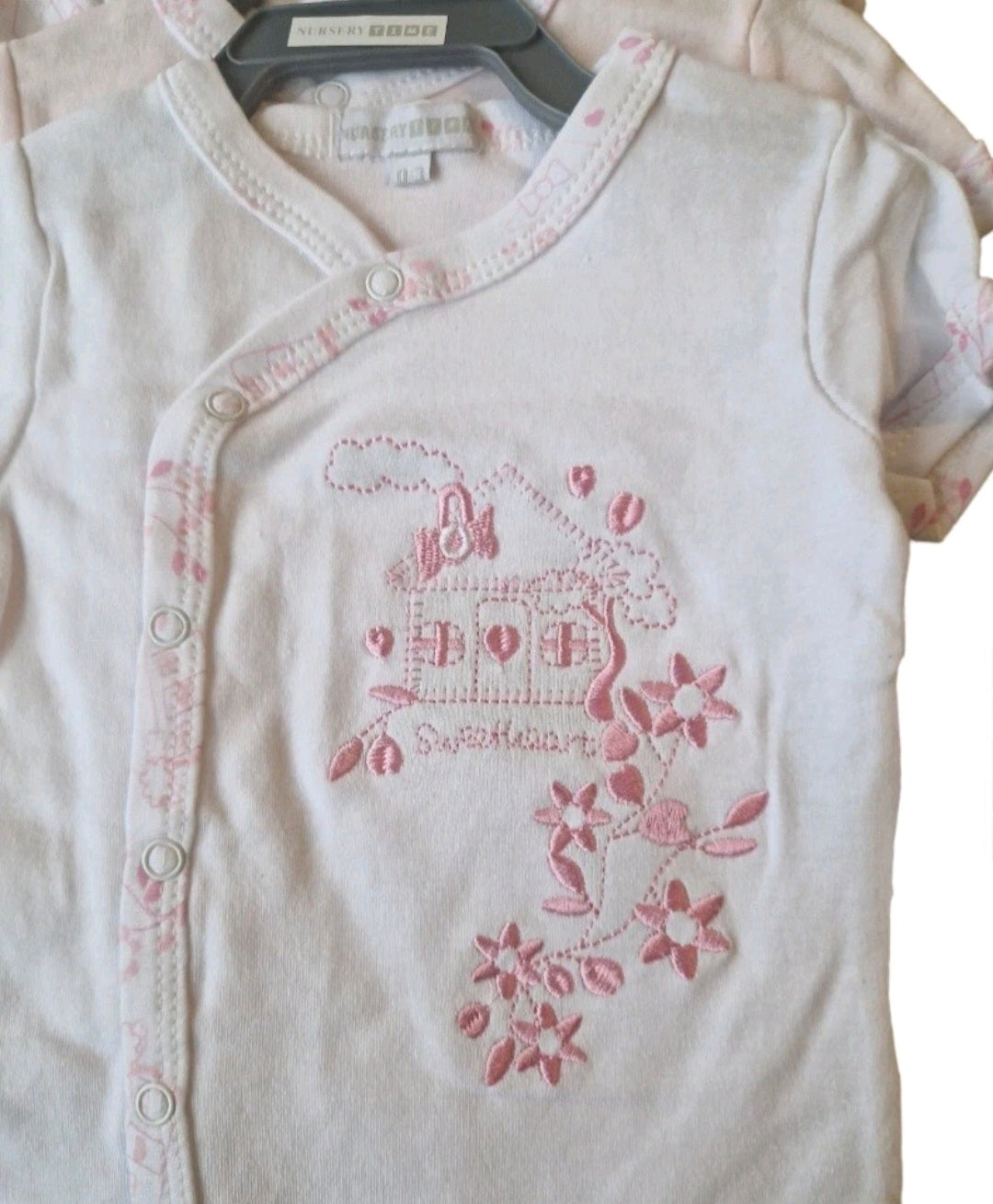 White baby outfit with pink floral embroidery on a white background