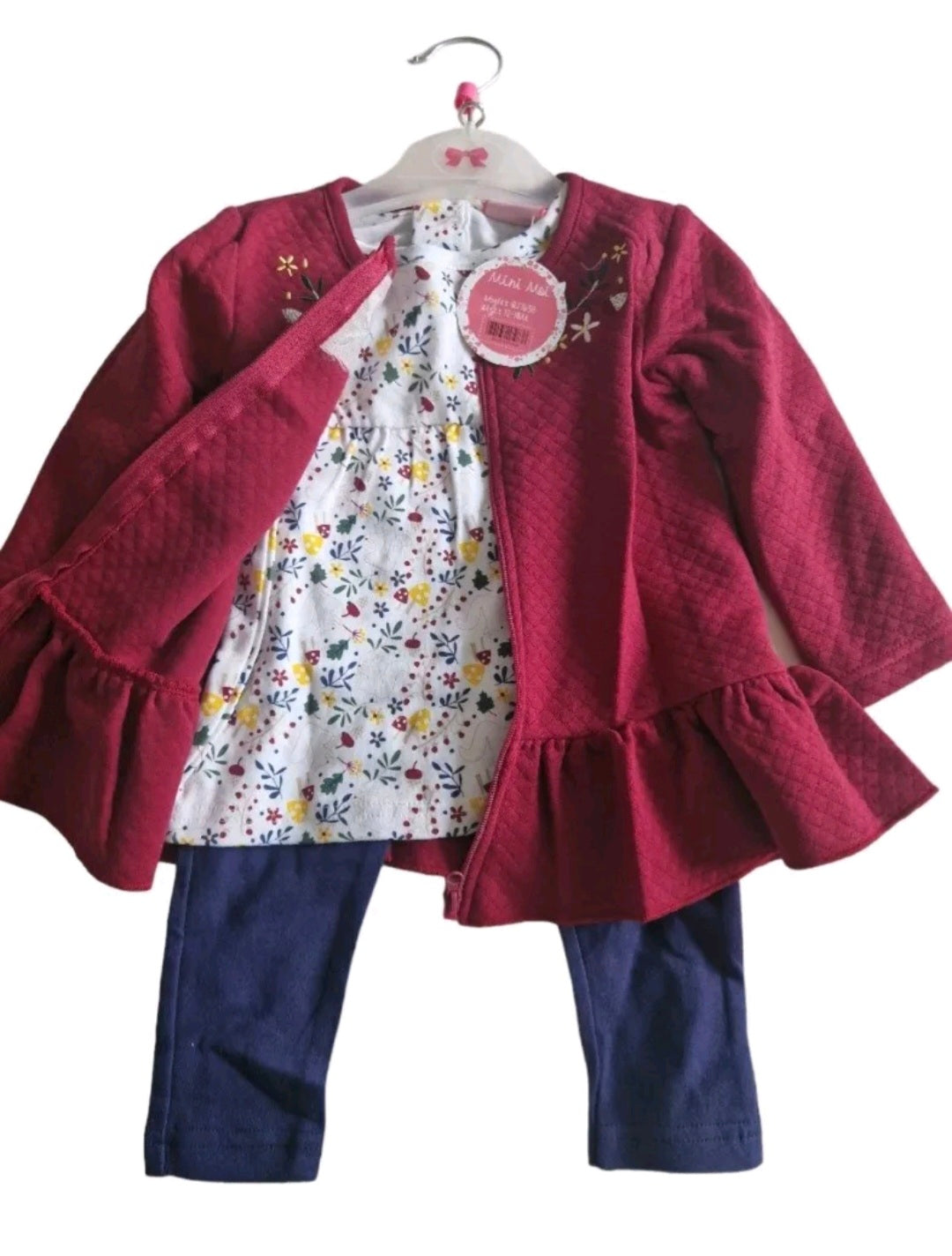 Children's outfit with red cardigan, floral dress, and blue pants on a white background