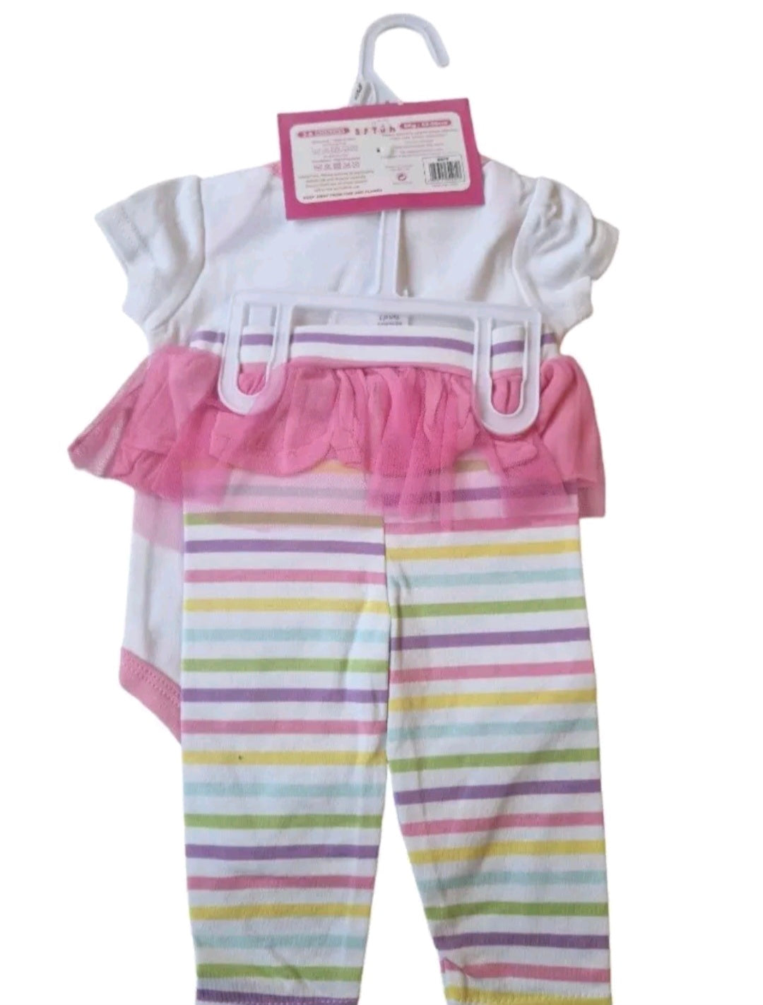 Baby outfit with white top and pink ruffled shorts with colorful striped pants on a hanger.