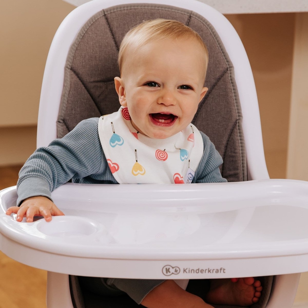 Baby sitting in a high chair with a Kinderkraft brand label, smiling.