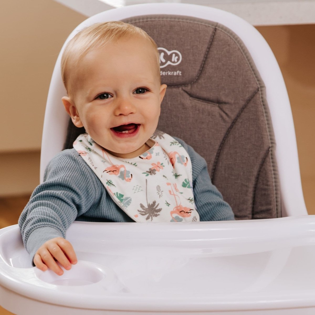Child in a high chair with a bib, smiling indoors