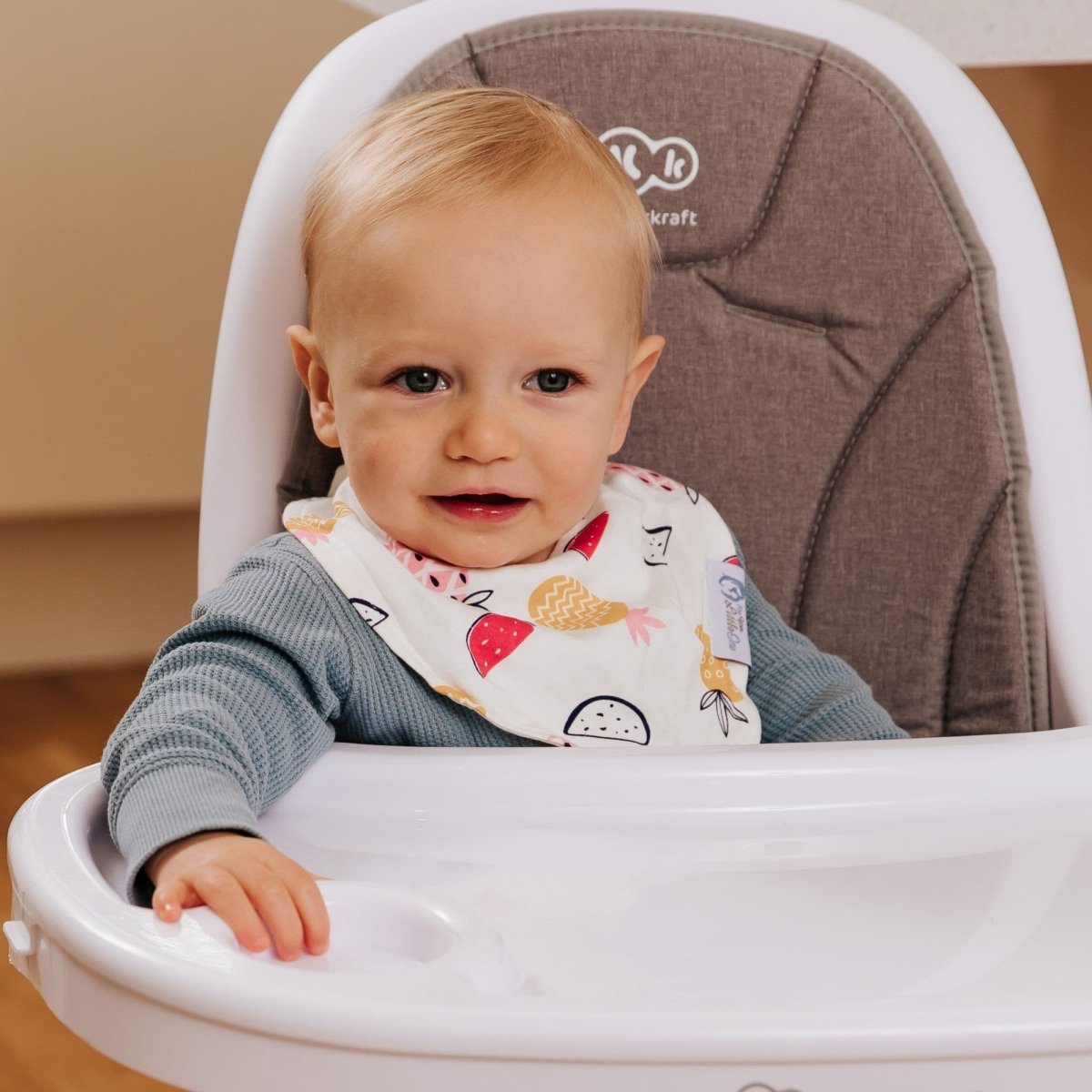 Baby sitting in a high chair wearing a bib with fruit patterns