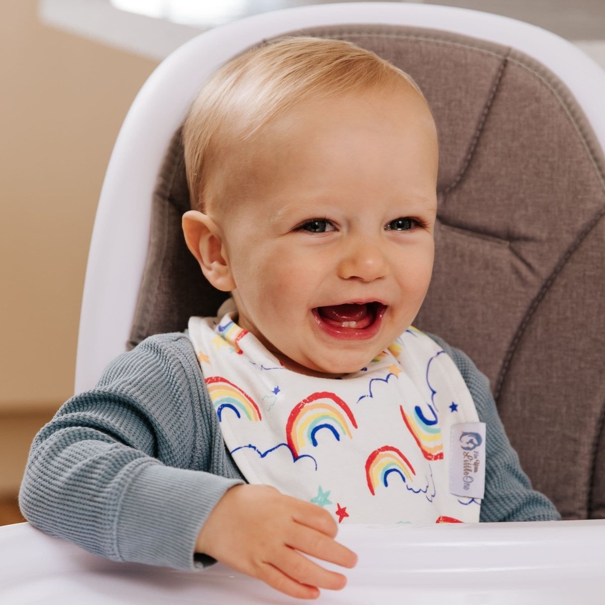 Child wearing a bib with rainbow patterns in a high chair