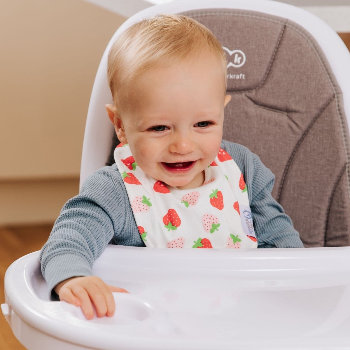 Child wearing a strawberry-patterned bib sitting in a high chair.