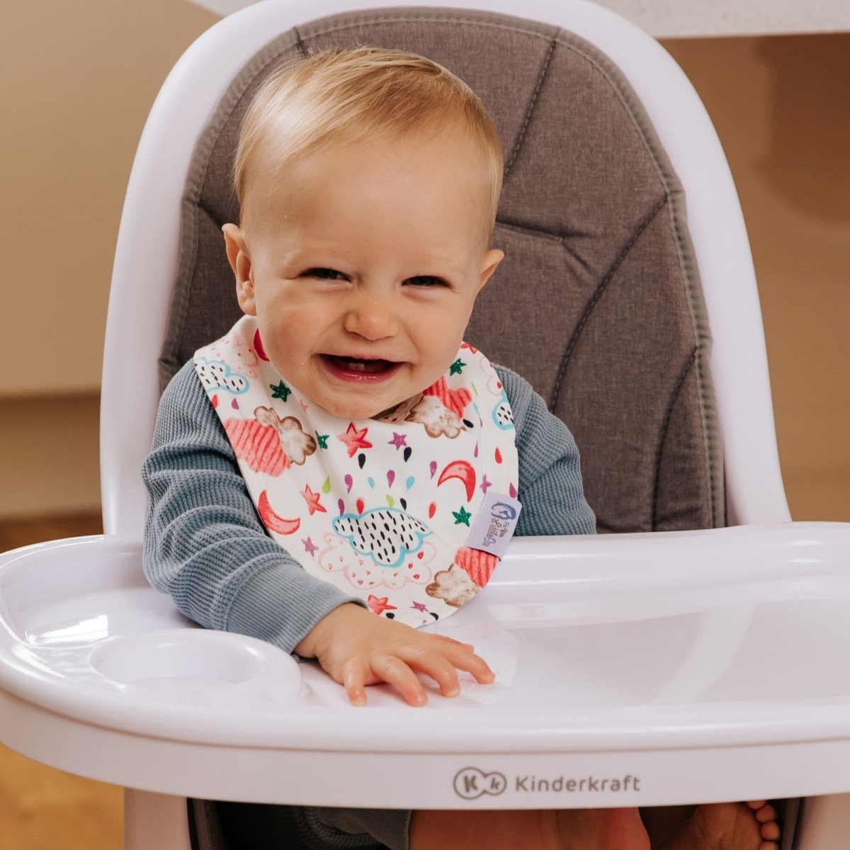 Child in a high chair wearing a colorful bib, with a blurred background