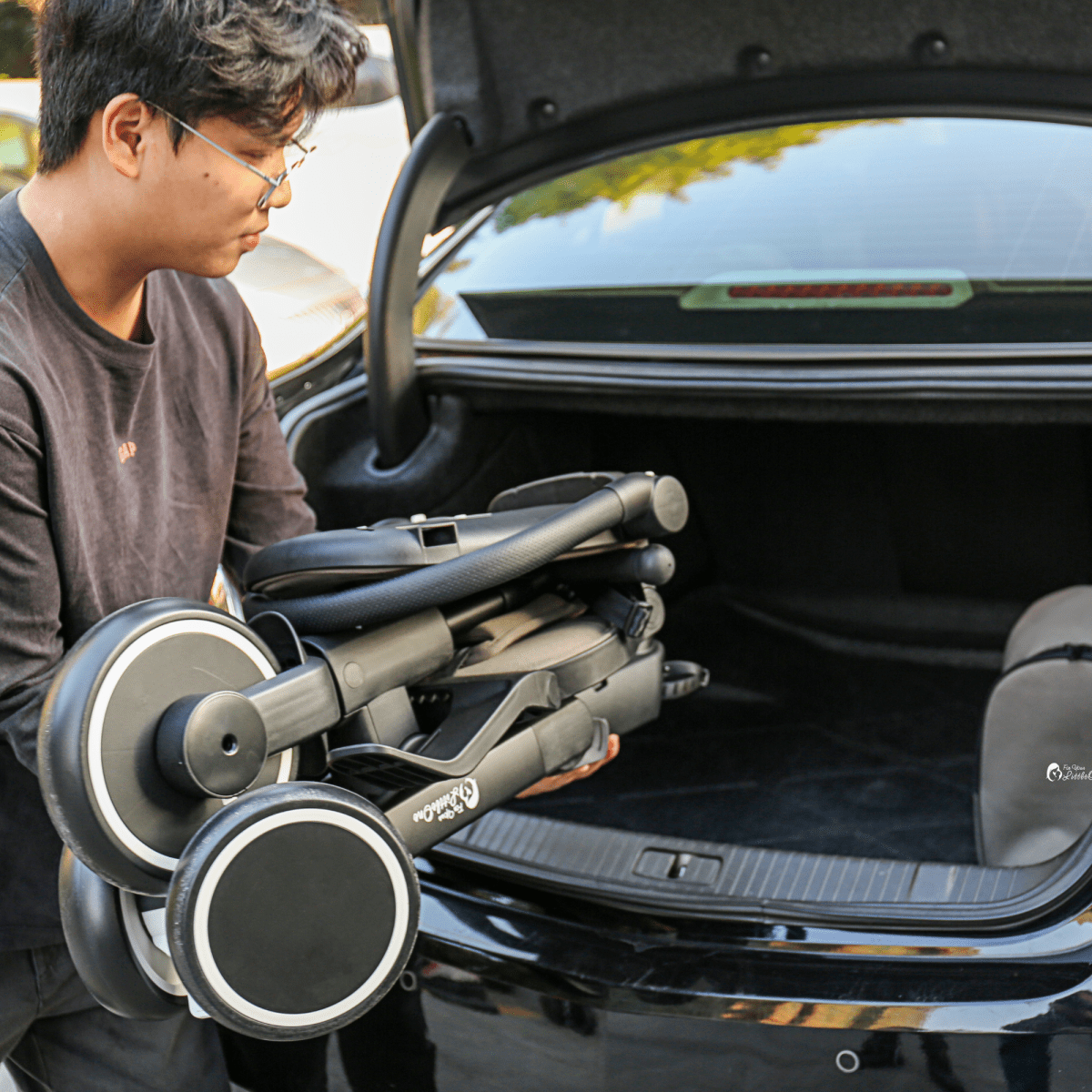 Person loading a folded baby stroller into a car trunk