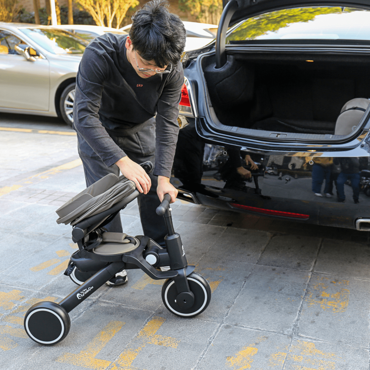 Person loading a stroller into a car trunk on a city street.
