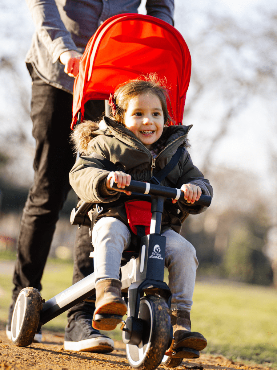 Child riding a scooter with a red canopy in a park