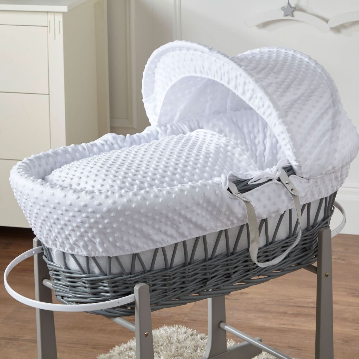 Gray wicker baby Moses basket with white hood and lining on a wooden floor.