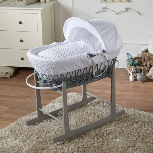 Gray wicker Moses basket with white hood and mattress on a stand in a nursery.